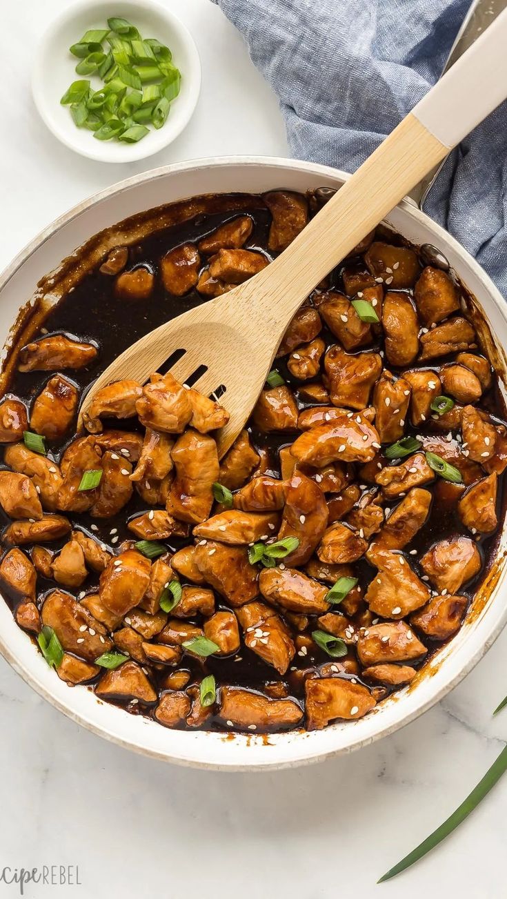 the chicken dish is being cooked in a skillet with a wooden spoon on top