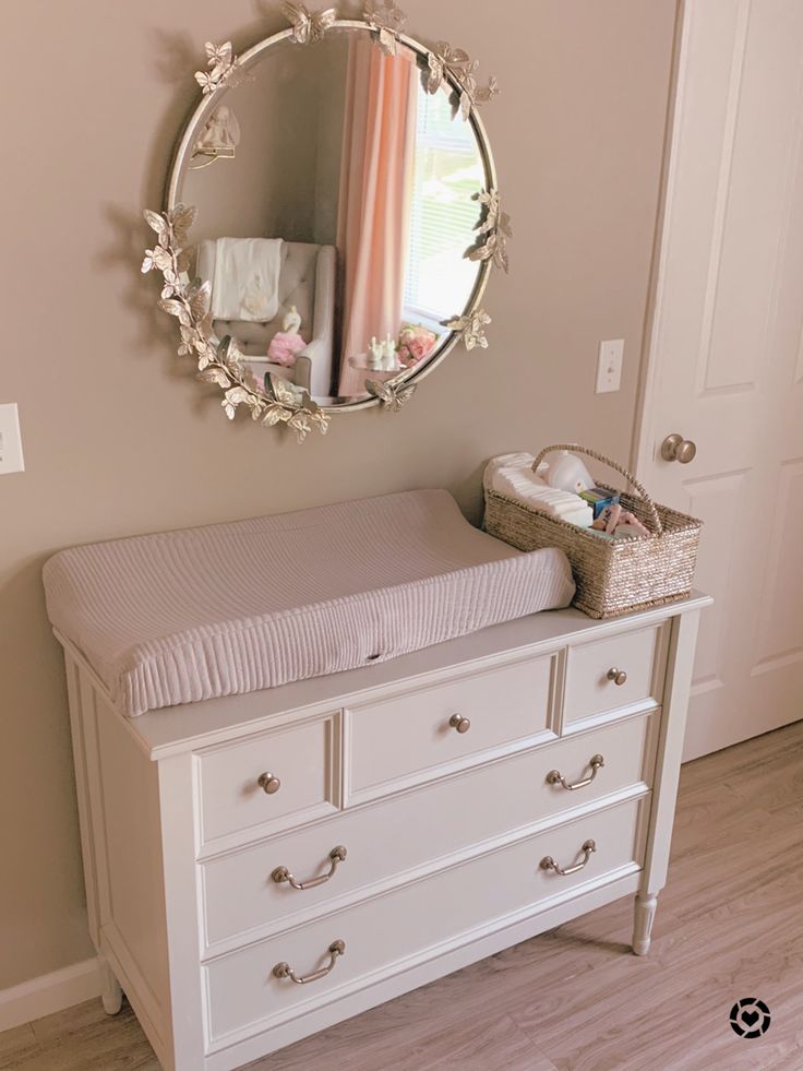 Photo shows a baby girls nursery. It shows a grey changing table and above it has a round mirror with its edges covered in butterflies. The grey tufted rocking chair across the room is caught in the reflection of the mirror. Butterfly Baby Room, Organization Nursery, Girly Nursery, Girl Nursery Themes, Butterfly Nursery, Baby Room Themes, Nursery Closet