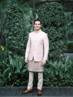 a man standing in front of some bushes wearing a tan suit and brown dress shoes