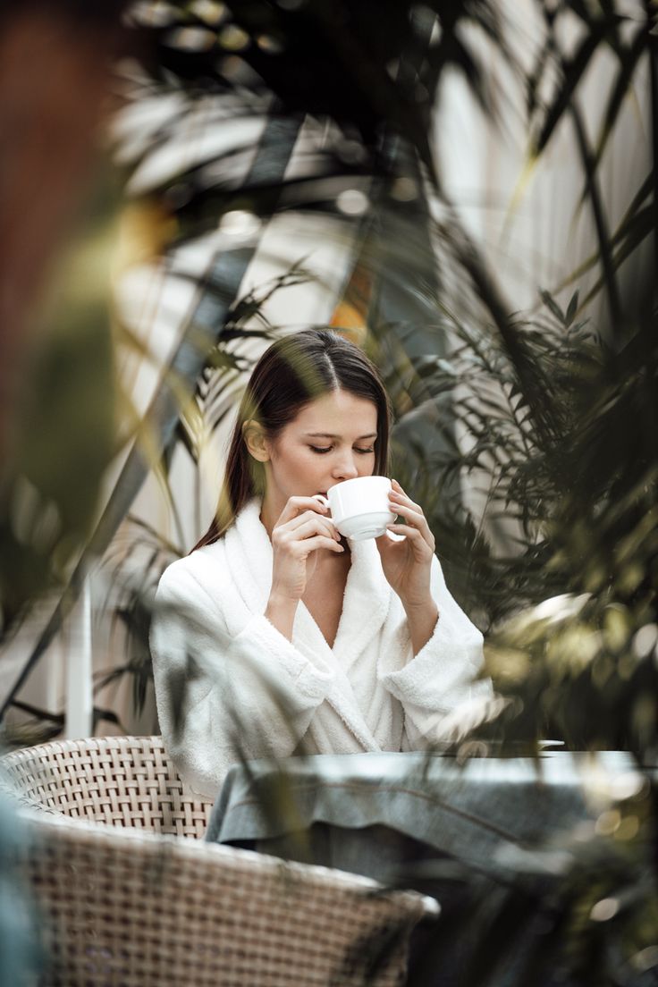 a woman sitting at an outdoor table drinking from a coffee cup in front of her