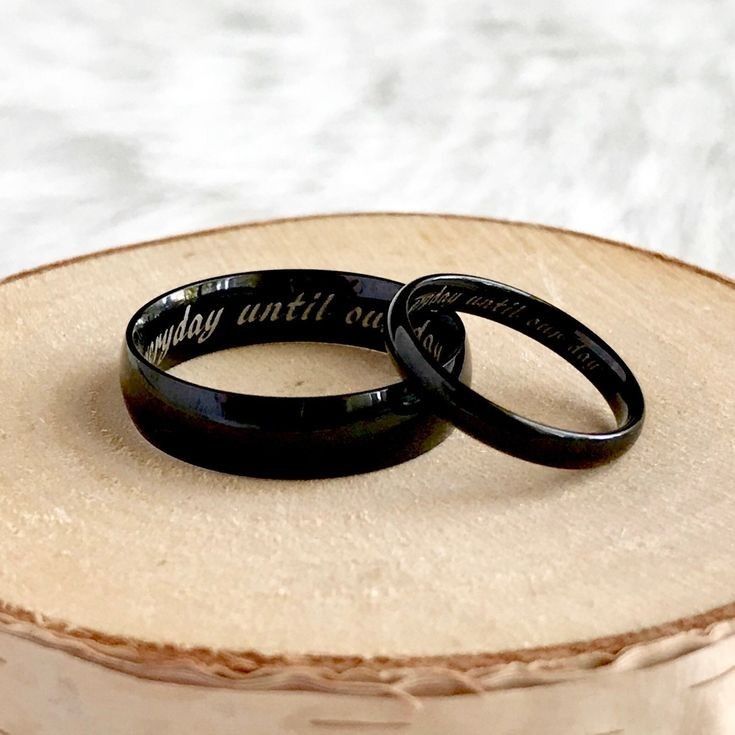 two black wedding rings sitting on top of a piece of wood