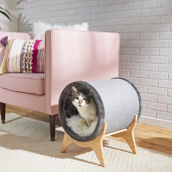 a cat sitting in a tunnel on the floor next to a pink couch