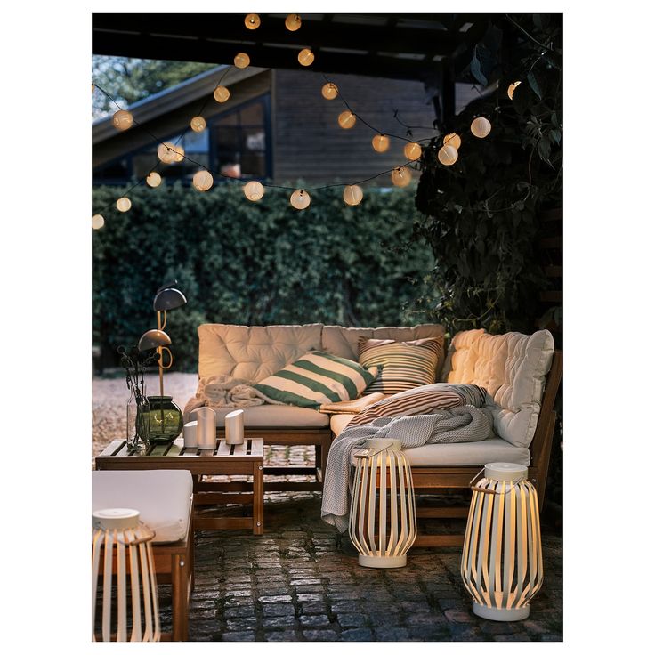 an outdoor living room with lights strung over the couches and table in front of it