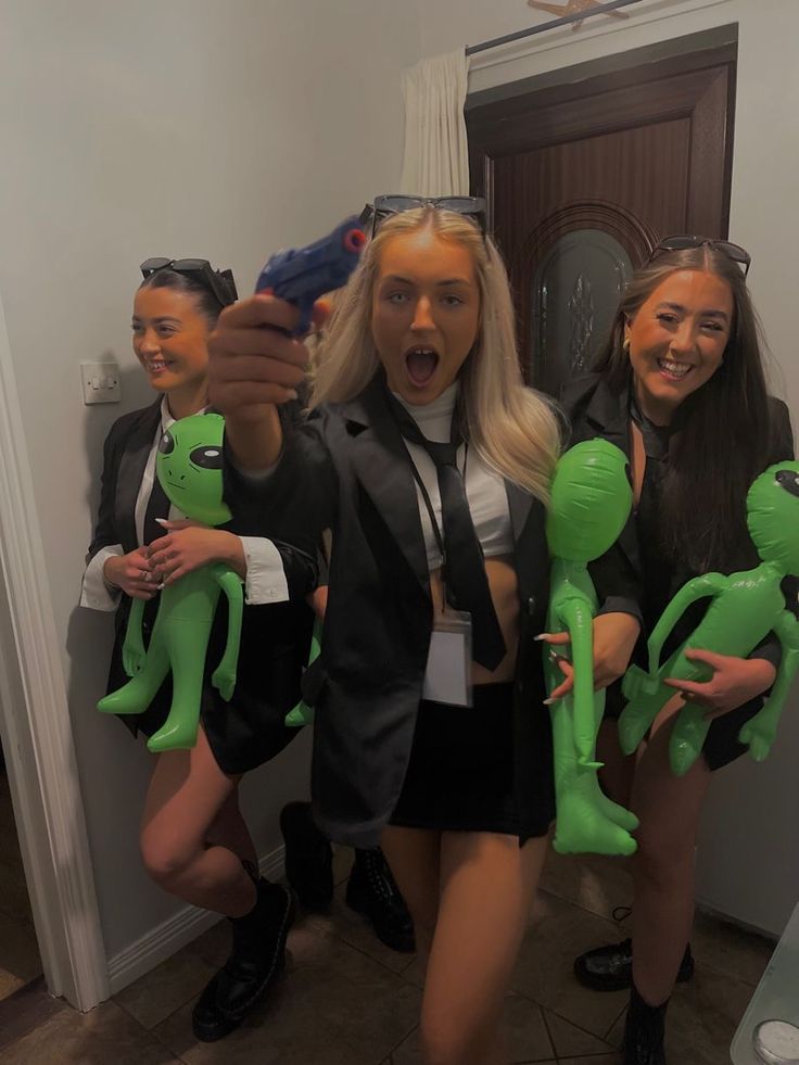 three women dressed up as alien dolls posing for the camera with one holding a toy