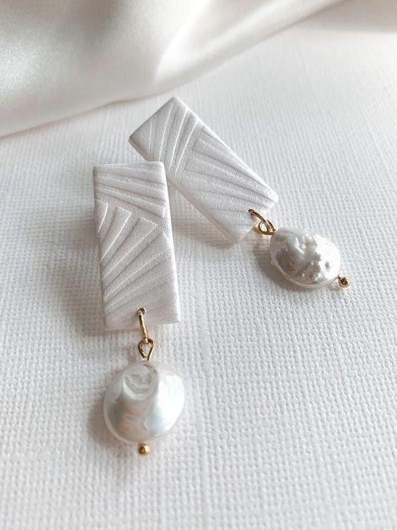 two pairs of earrings with pearls hanging from them on a white cloth covered tablecloth