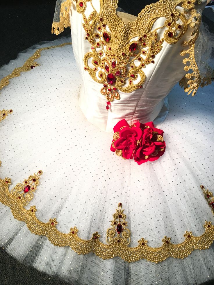 a white tutu with gold trim and red flowers on the bottom, sitting on a black surface