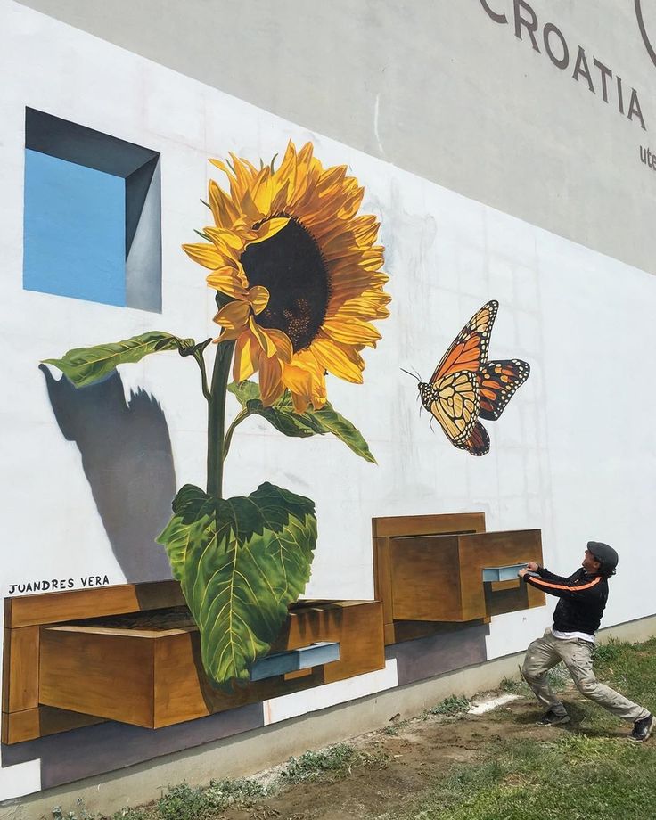 a man is painting a mural on the side of a building with sunflowers and butterflies