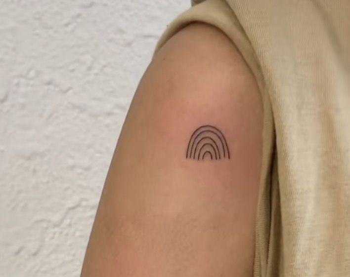 a person's arm with a small rainbow tattoo on the left side of their arm