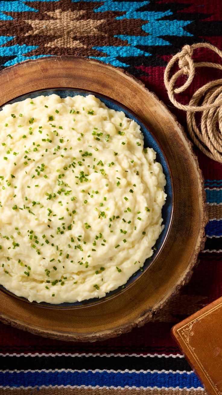 mashed potatoes in a wooden bowl on a colorful tablecloth next to twine of twine