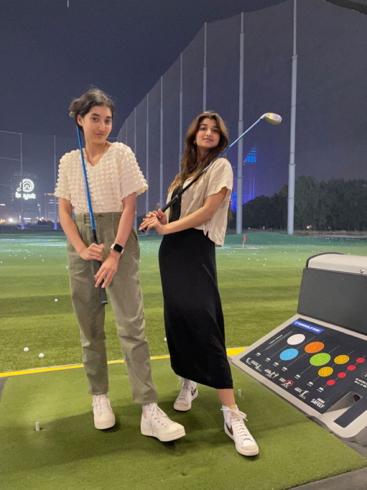 two women standing next to each other in front of an interactive golf game on the field