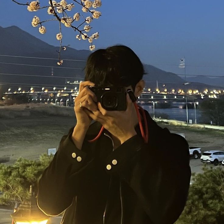 a man taking a photo with his camera in front of a flowering tree at night