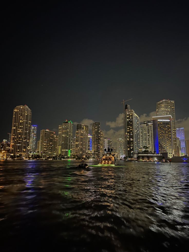 the city skyline is lit up at night with lights reflecting off the water in front of it