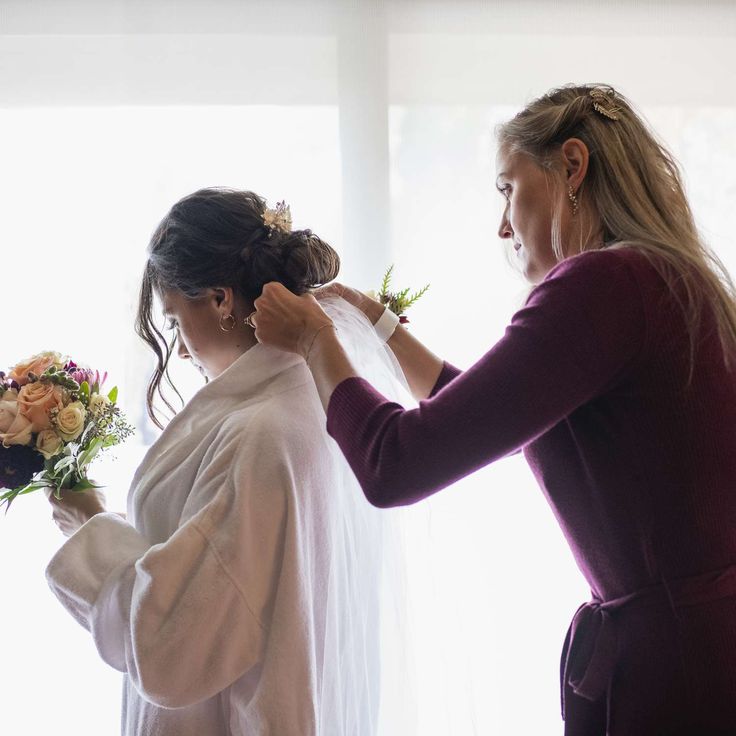 two women standing next to each other in front of a window with flowers on it