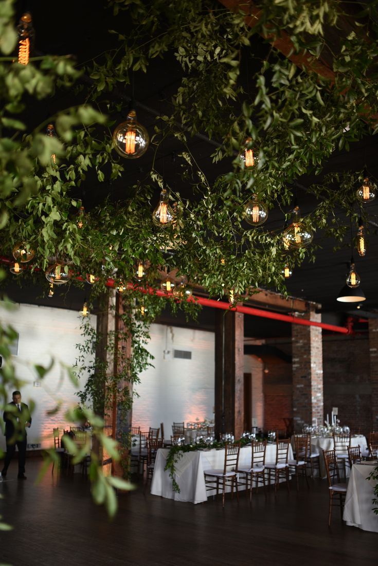 the tables are set up with white linens and greenery hanging from the ceiling