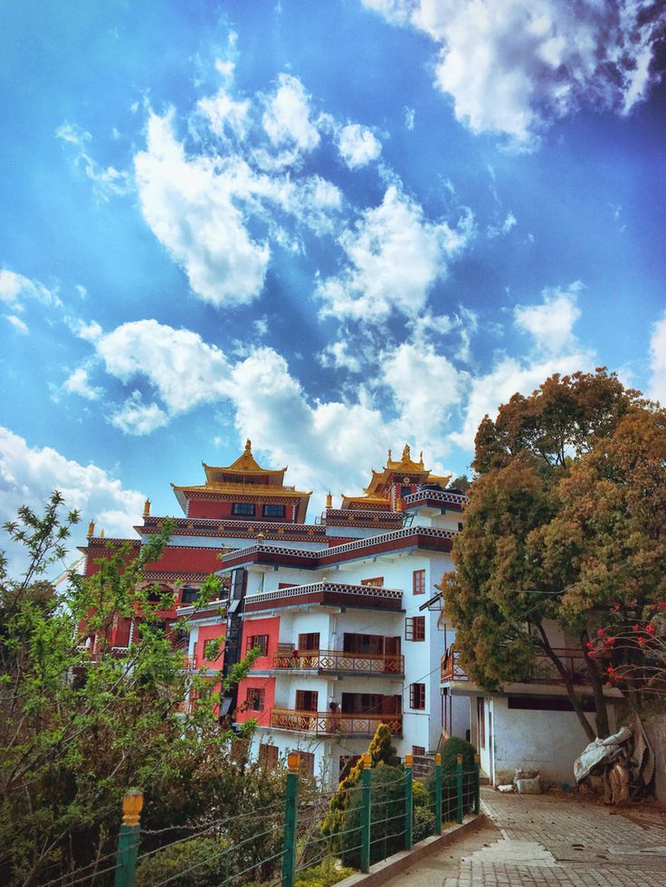 a large white building sitting next to a lush green forest under a cloudy blue sky