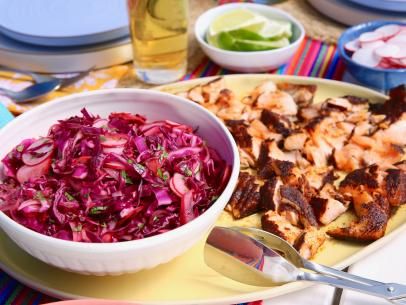 a bowl of red cabbage next to a plate of food on a table with utensils