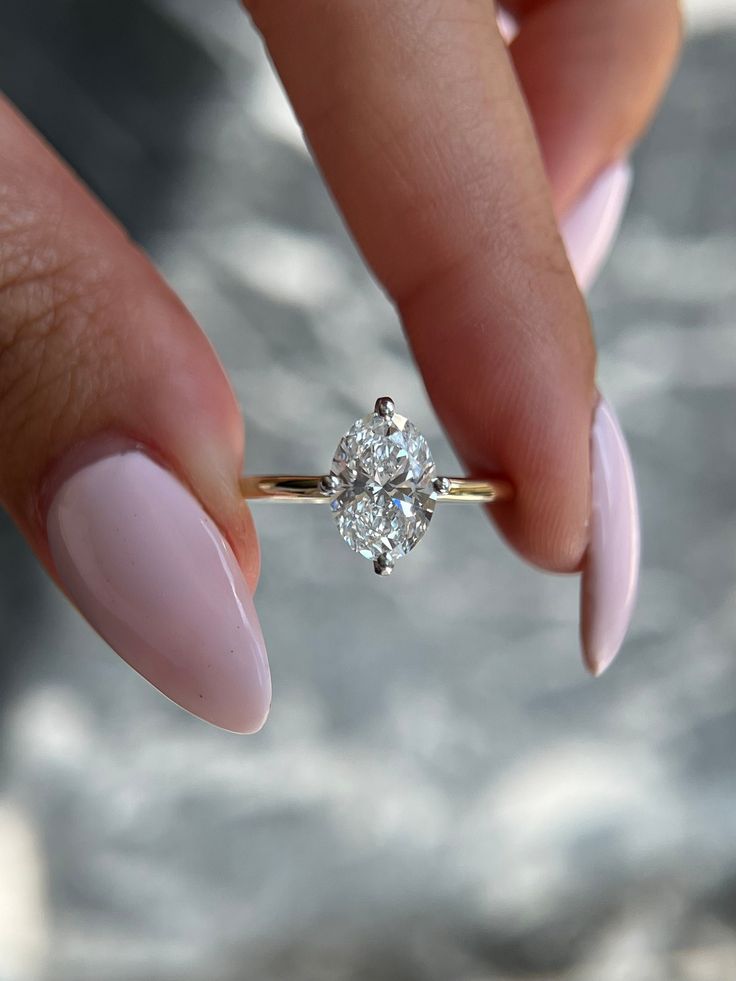 a woman's hand holding a ring with a diamond on it and the tip of her finger