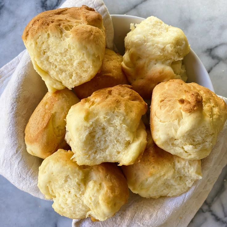 a white bowl filled with biscuits sitting on top of a marble countertop next to a napkin