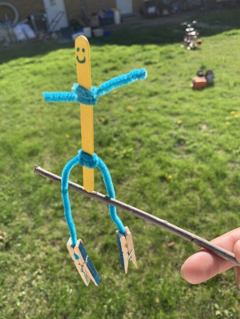 a person holding up a toy made out of sticks and scissors in the grass with text overlay reading how to make a scarecrow