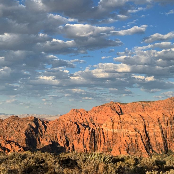 the mountains are covered in red rock under a blue sky with white clouds above them