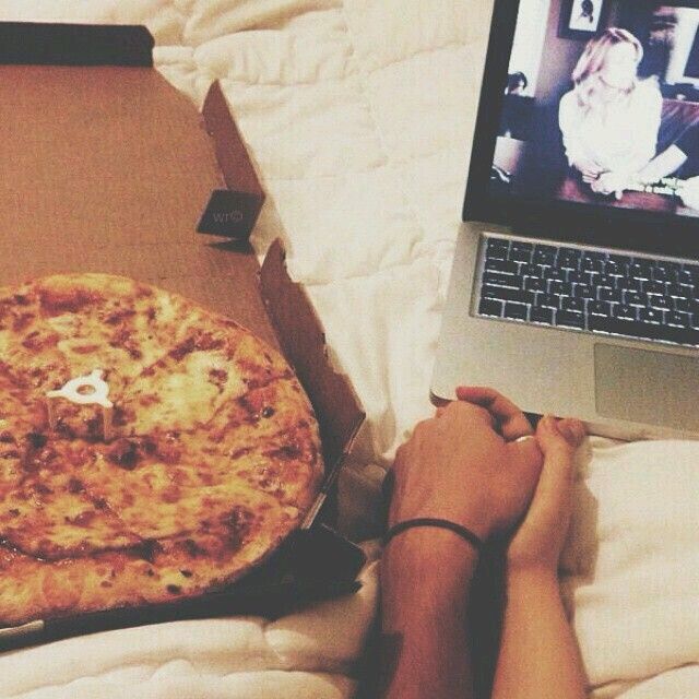 a person laying in bed next to a laptop with a pizza on top of it