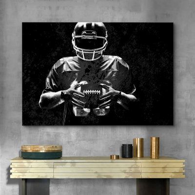 a black and white photo of a football player holding a ball on a wall above a console table