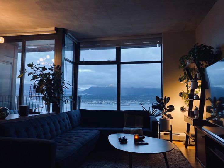 a living room filled with furniture and a large window overlooking the water at night time