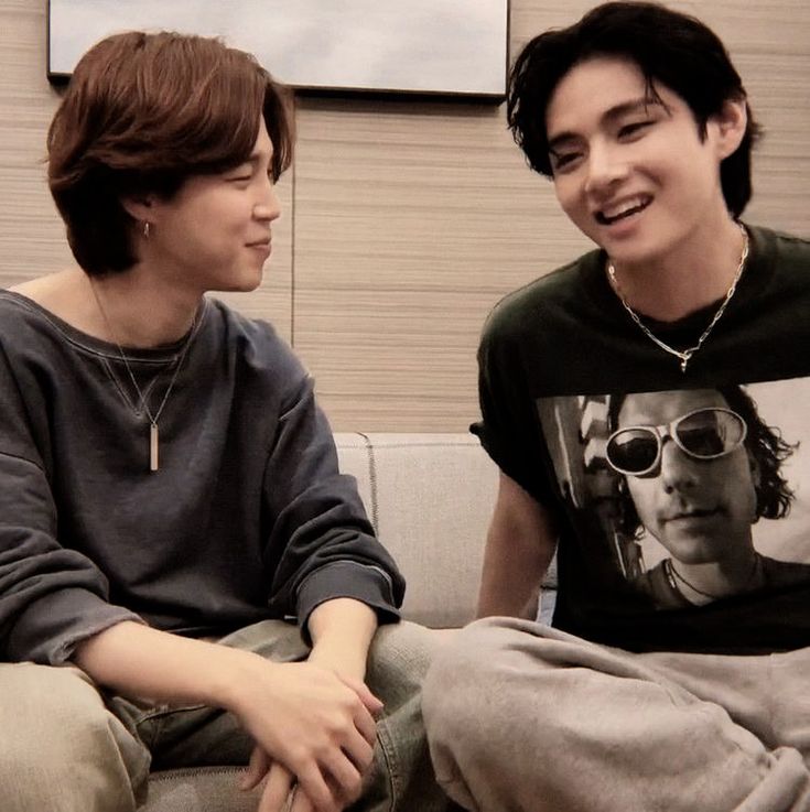 two young men sitting on top of a couch next to each other, one smiling