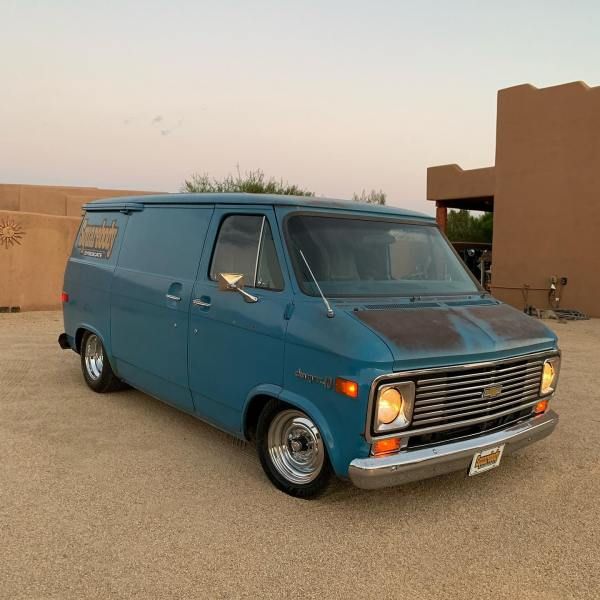 an old blue van parked in front of a building with a desert landscape behind it