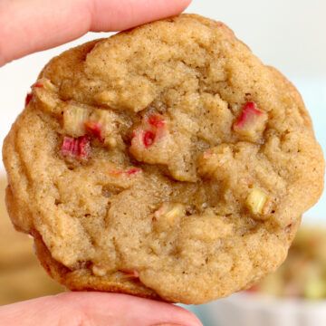 a close up of a person holding a cookie in their hand with cranberry toppings on top