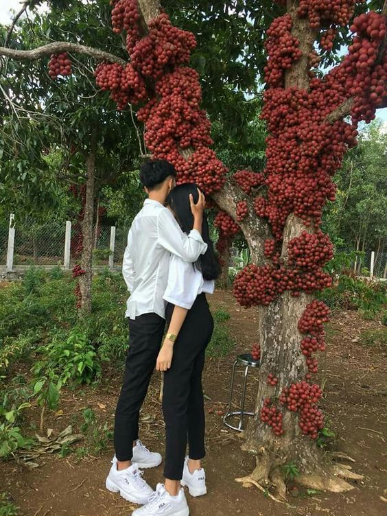 two people standing next to each other in front of a tree with red berries on it