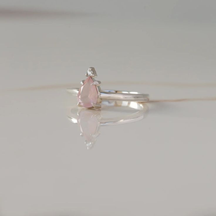 A ring that reminds you of the queen that you are? A pear-shaped Rose Quartz topped with a round Moissanite is giving us full-on royal vibes and we are loving it. A little treat-yourself gift never hurt nobody! Details: Center stone Gemstone: Rose Quartz Stone Shape: Pear Measurements: approx. 7x5mm Side stones Gemston Pear-shaped Birthstone Promise Ring, Pear-shaped Rose Cut Diamond Rings For Proposal, Pear Shaped Rose Cut Diamond Ring For Proposal, Pear-shaped Rose Cut Diamond Proposal Ring, Teardrop Solitaire Ring For Proposal, Teardrop Rose Cut Diamond Promise Ring, Fine Jewelry Teardrop Crystal Ring As Gift, Teardrop Crystal Ring Fine Jewelry Gift, Sterling Silver Pear-shaped Diamond Ring As Gift