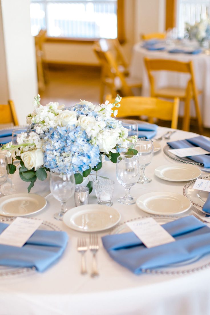 the table is set with blue and white place settings, silverware, and flowers