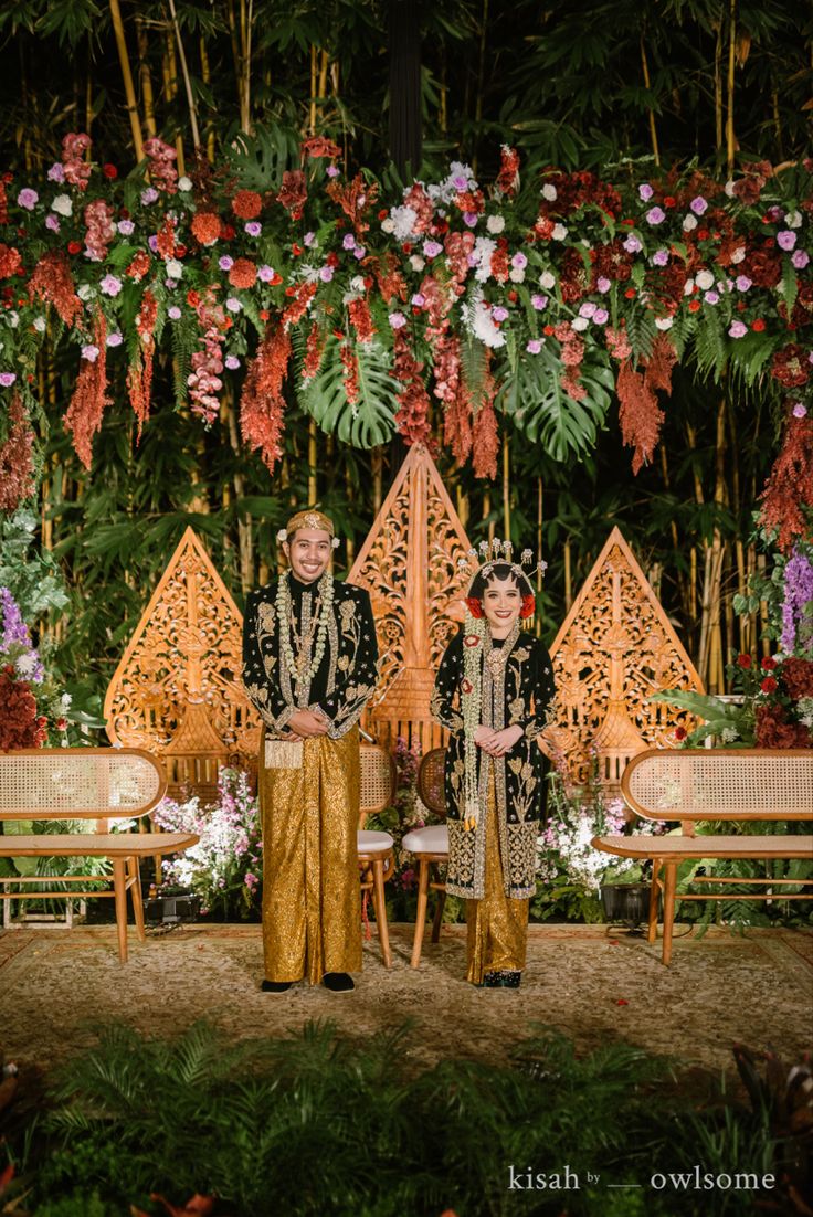 two people sitting on chairs in front of flowers and greenery at an outdoor wedding