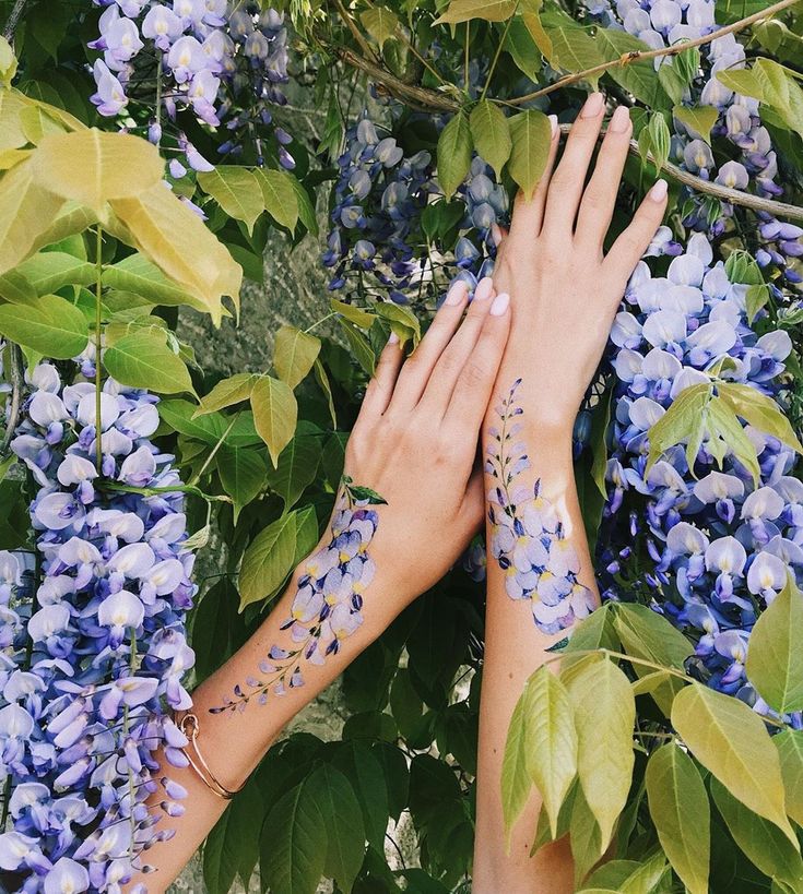 two hands touching each other in front of purple flowers and green leaves on the branches