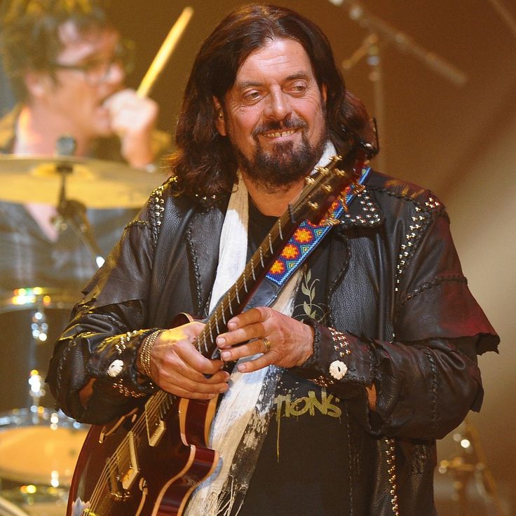 a man with long hair and beard holding a guitar in front of him on stage