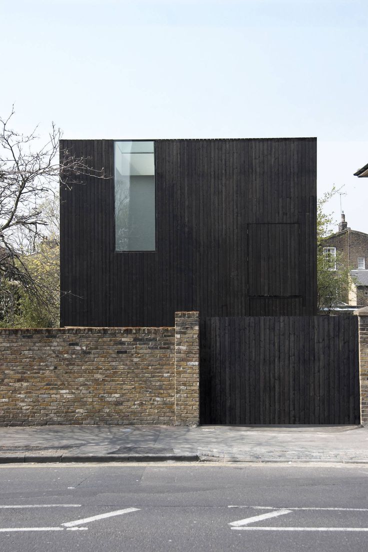 a black building on the side of a road next to a brick wall and trees