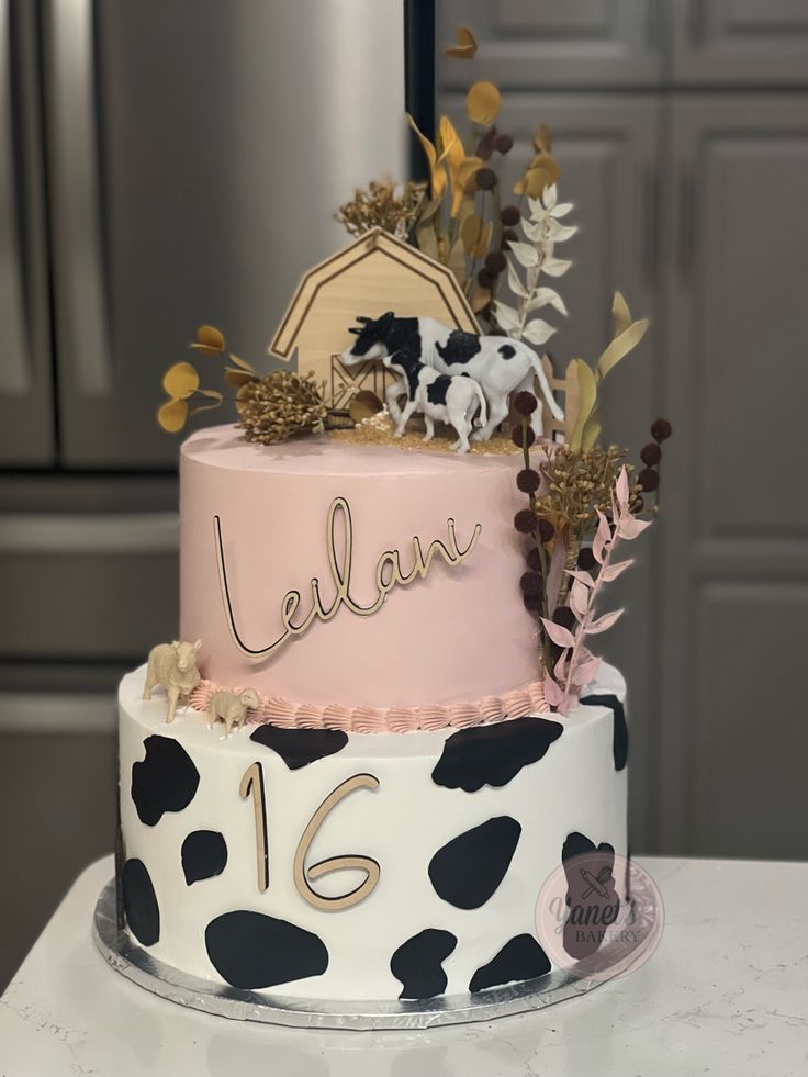 a cake decorated with black and white cow prints, gold leafy decorations, and the number 16