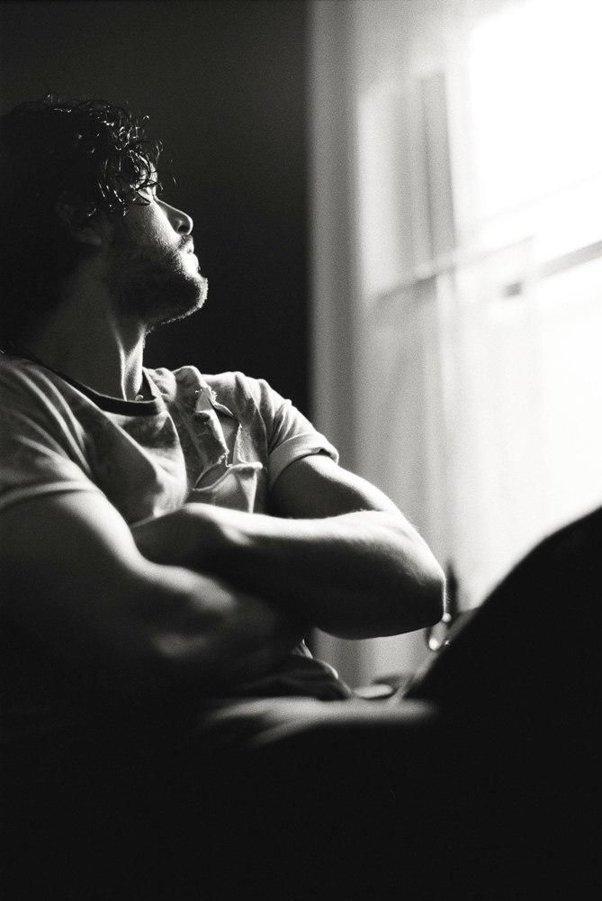 a black and white photo of a man with his arms crossed looking out the window