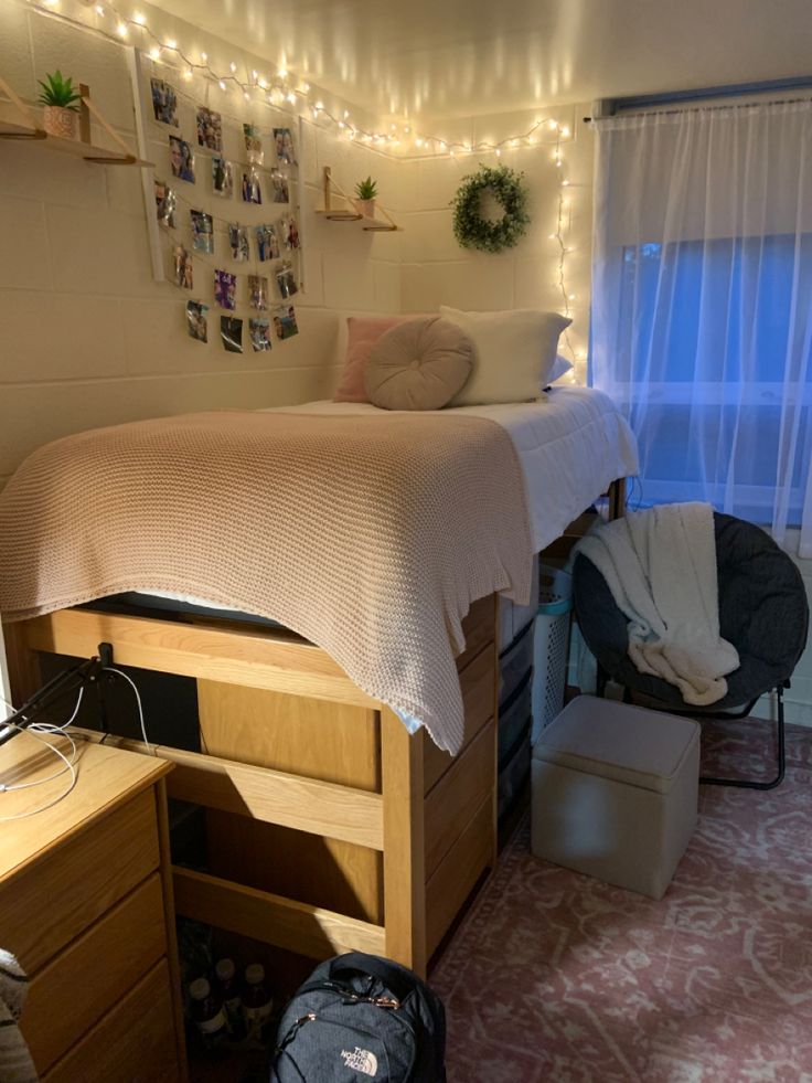 a dorm room with a bed, desk and chair next to a window covered in fairy lights