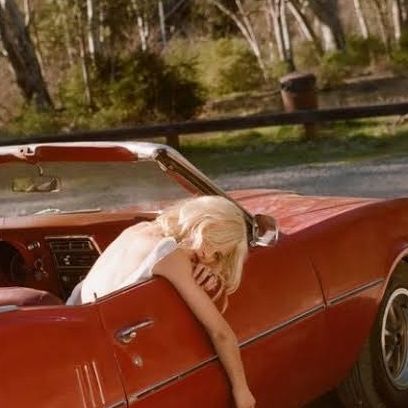 a woman leaning on the hood of an old red car with her head sticking out