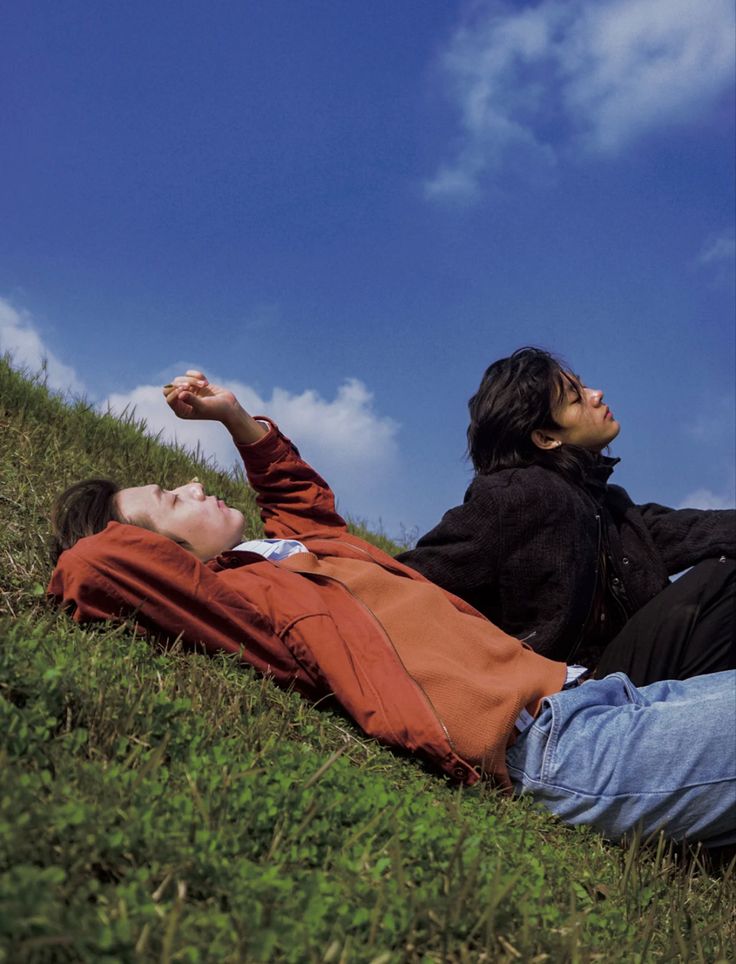 two people laying in the grass on a hill