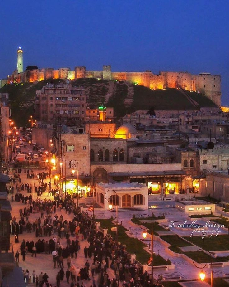 the city is lit up at night and people are walking around in the street below