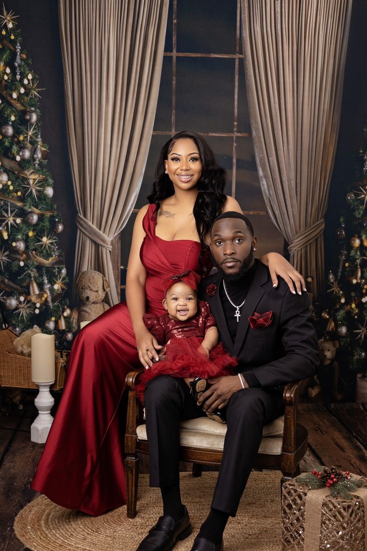 a man and woman sitting next to a baby in a chair with christmas decorations on the wall behind them