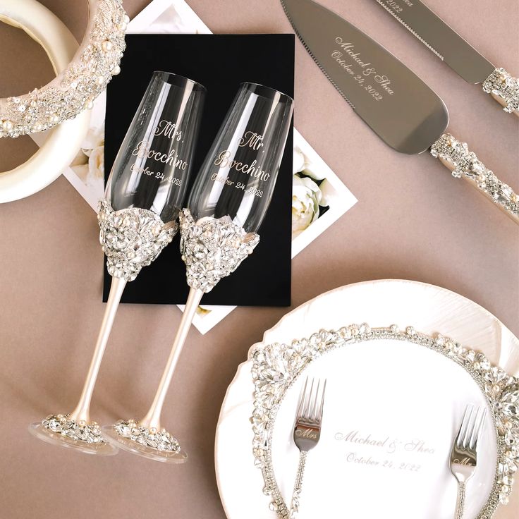 two champagne flutes are sitting on a table next to silverware and napkins with the names of bride and groom