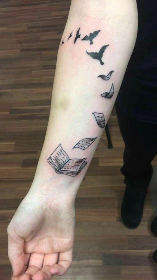 a person with a book and birds tattoo on their arm that is flying in the air