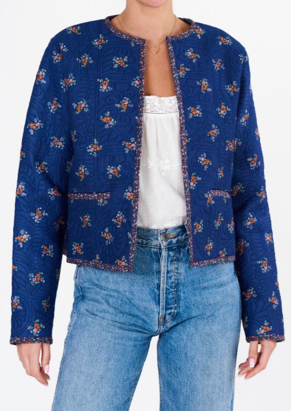 a woman is wearing a blue jacket with flowers on it and she has her hands in her pockets