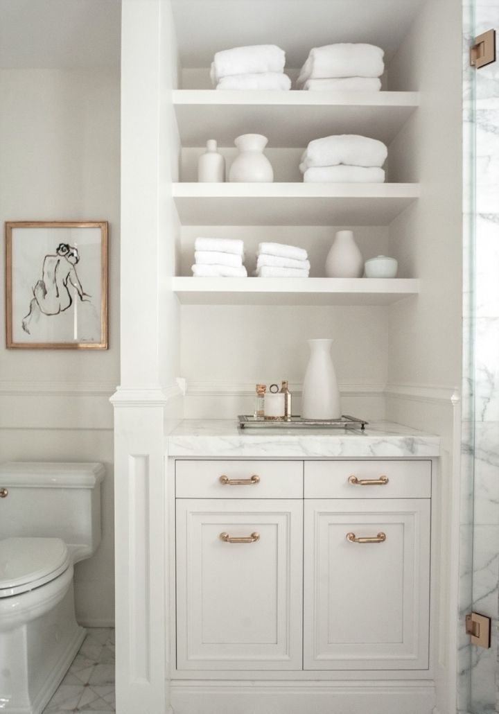 a white bathroom with marble counter tops and shelves filled with towels, vases, and other items