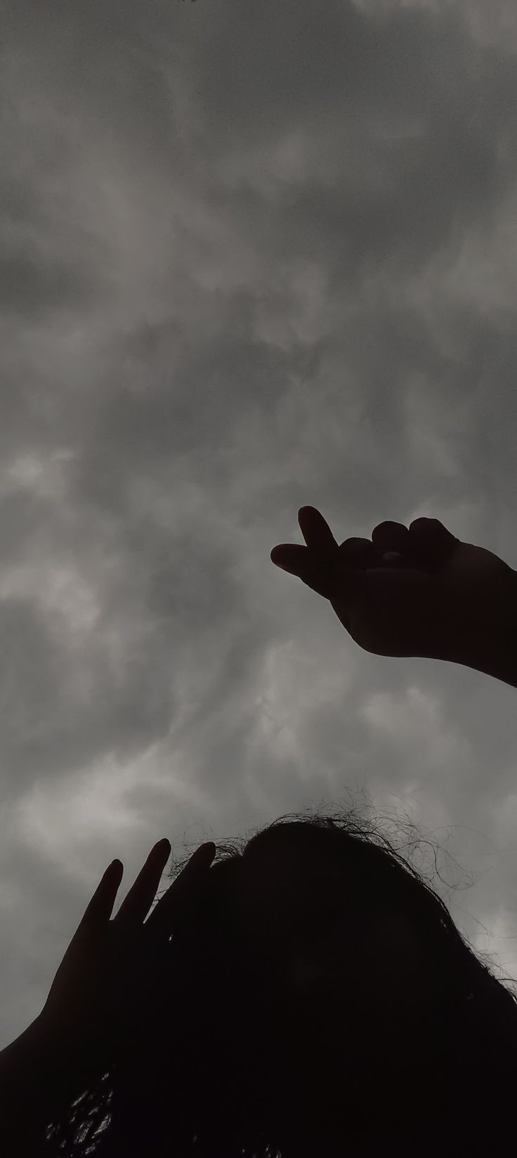 the silhouette of a person's head and hand reaching up towards an object in the sky