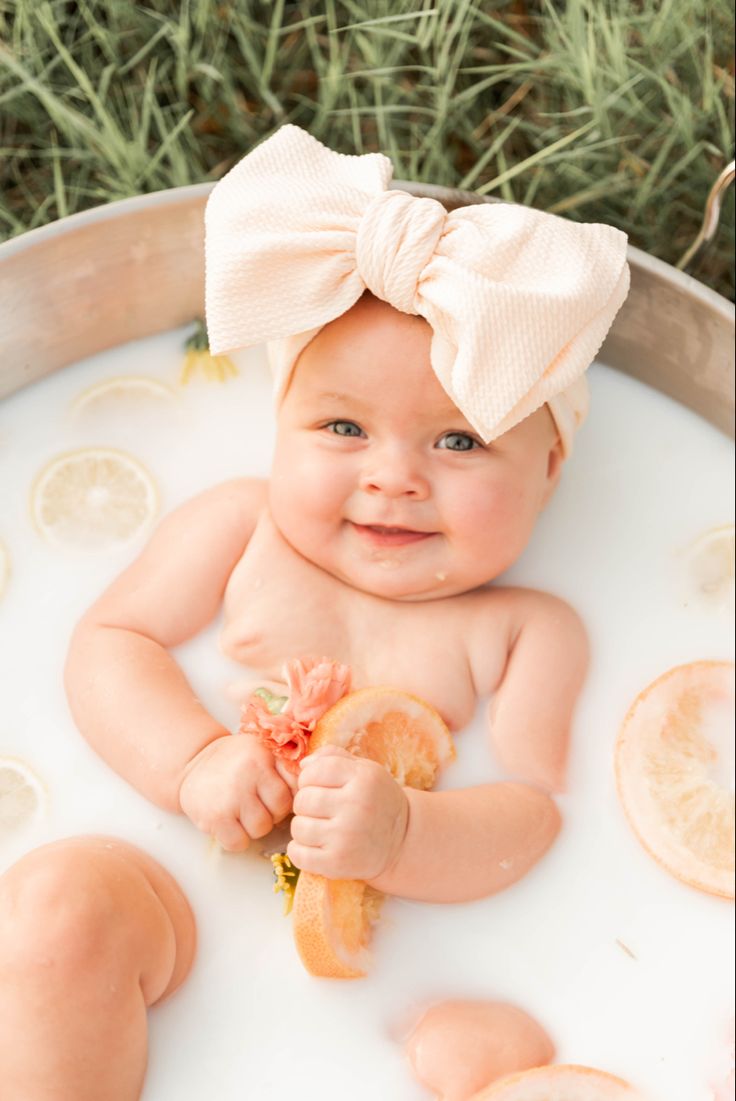 a baby in a tub with lemons and a bow on her head, smiling at the camera